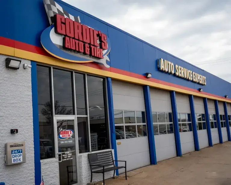 Blue and yellow auto service shop with Gordies Auto & Tire sign above several garage doors. A bench and 24/7 drop box are by the entrance. Auto Service Experts is displayed in yellow letters above the garages.